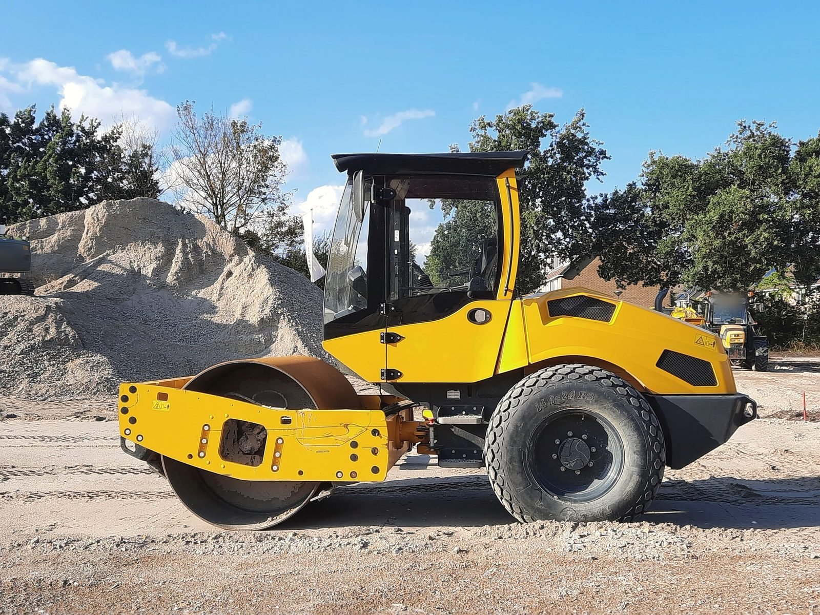 A compactor parked by graded stockpiles of stone and gravel.