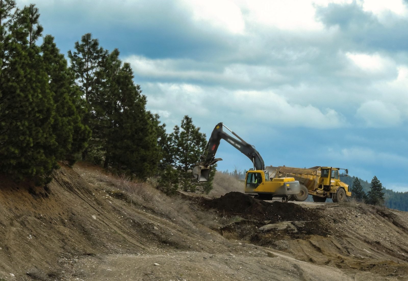 An excavator loads a dump truck on a graded slope.